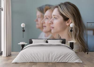 Women of three female family generations side portrait. Serious young adult granddaughter, mature mother, senior grandmother standing in row, line, looking at forward, thinking of dynasty, heredity Wall mural