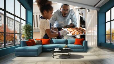 Wow, looks great. Excited caring millennial african dad or grown elder brother watching concentrated small black daughter or younger preteen sister taking pan with self baked tasty muffins out of oven Wall mural