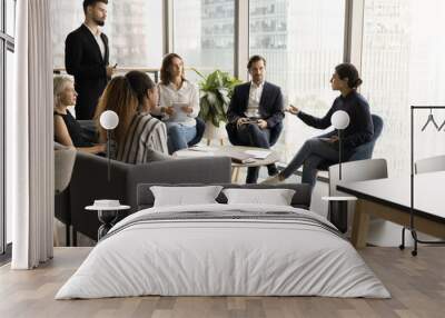 Young Indian business professional speaking on team brainstorming meeting in office lobby, offering ideas for plan, strategy to male boss, talking to diverse group of colleagues Wall mural