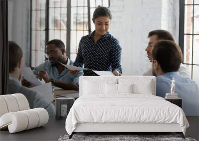 Young Indian businesswoman lead meeting with diverse colleagues share handouts at briefing, confident female biracial team leader head team discussion in office, consider paperwork with coworkers Wall mural