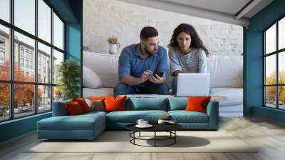 Young multi ethnic spouses sit at table pay bills on-line using laptop, counting earnings and monthly expenses engaged in budget control, reviewing utilities. Manage family finances, planning concept Wall mural