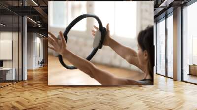 Young sporty attractive woman doing pilates toning exercise for arms and shoulders with ring, fitness with pilates magic circle in hands, working out, indoor close up. Strength, well being concept Wall mural