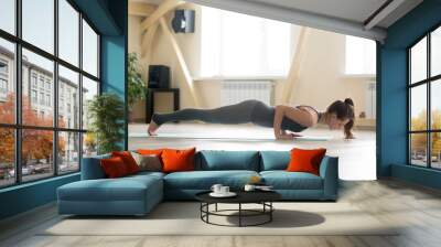 Young sporty happy woman practicing yoga, doing Push ups or press ups exercise, four limbed staff chaturanga dandasana pose, working out wearing grey sportswear, indoor full length, home or sport club Wall mural