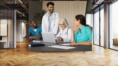 Young team medics interns medical faculty students gather on seminar training holding by mature female doctor professor. Multicultural teammates listen to leader analyzing clinical case using laptop Wall mural