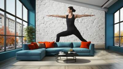 Young yogi attractive woman practicing yoga concept, standing in Warrior Two exercise, Virabhadrasana II pose, working out, wearing sportswear, black tank top and pants, full length, white loft Wall mural