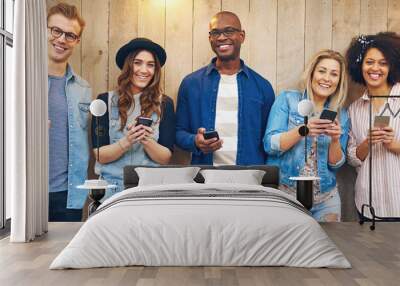 Cheerful multiethnic friends looking at camera standing with phones Wall mural