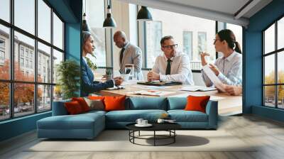 Diverse group of businesspeople talking together around an office table Wall mural