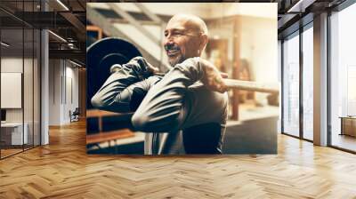 Fit mature man lifting weights and smiling in a gym Wall mural