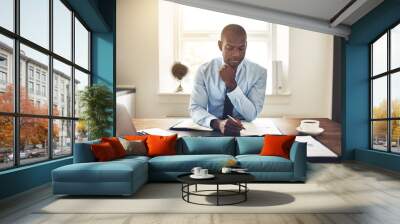 Focused young executive reading through paperwork at his desk Wall mural