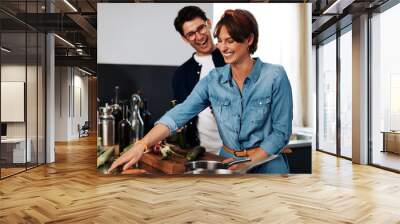 Laughing couple making dinner at home Wall mural