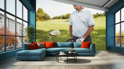 Senior man standing with his golf clubs on a fairway Wall mural