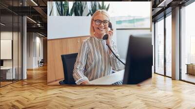 Smiling businesswoman sitting at her desk talking on a telephone Wall mural