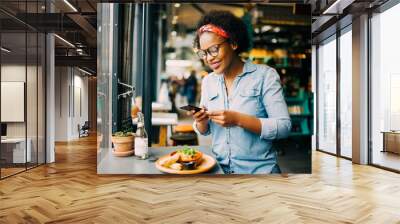 Smiling woman taking photos of her food in a cafe Wall mural