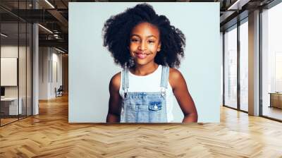 Smiling young African girl wearing dungarees against a gray back Wall mural