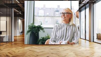 Smiling young businesswoman enjoying her coffee during an office break Wall mural