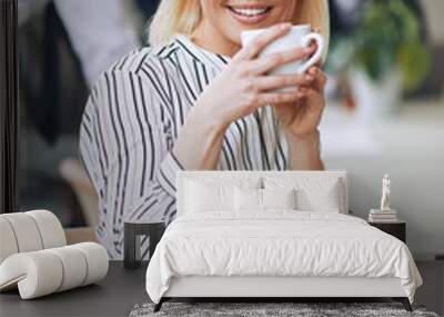 Smiling young businesswoman sitting at work drinking a coffee Wall mural