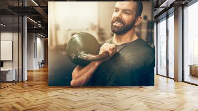 Smiling young man holding a dumbell at the gym Wall mural