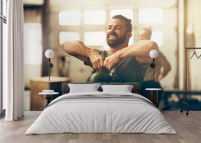 Smiling young man lifting a dumbbell while working out Wall mural