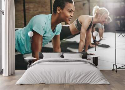 Smiling young woman doing pushups with friends at the gym Wall mural