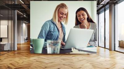 Two businesswomen sitting together in an office using a laptop Wall mural