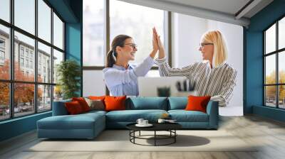 Two smiling businesswomen high fiving together in an office Wall mural