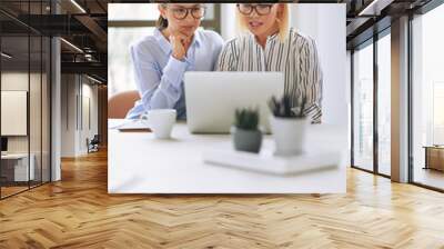 Two young businesswomen using a laptop together at work Wall mural