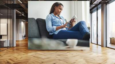 Young African woman sitting on her couch using a tablet Wall mural