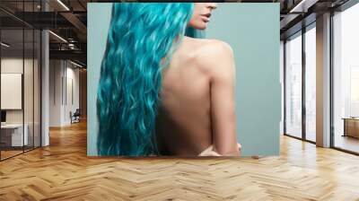 Beautiful woman with curly blue hair and tattoos posing at camera against blue background, back view Wall mural