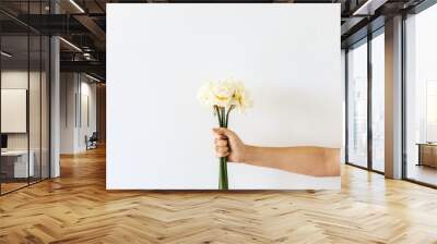 Female hand hold narcissus flowers bouquet on white background. Flat lay, top view minimal floral composition. Wall mural