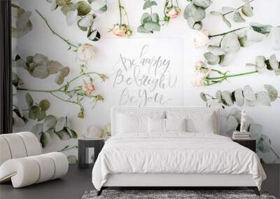 inspirational quote be happy, be bright, be you written in calligraphy style on paper with pink roses and eucalyptus branches on white background. flat lay, top view. Wall mural