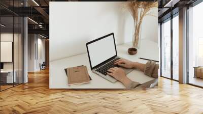 Office desk workspace with girl's, women's hands typing on laptop. Laptop computer with blank copy space display screen, notebook, reeds pampas grass bouquet. Wall mural