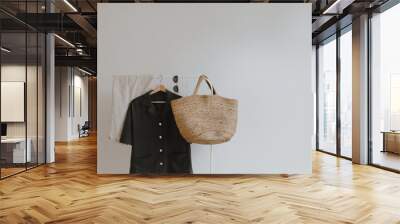 Trendy female wardrobe. Stylish women's summer clothes on hanger. Trousers, rattan bag, shirt, sunglasses Wall mural