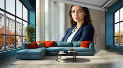 A confident young business woman in a blue suit standing with her arms crossed looking at the camera against a window Wall mural