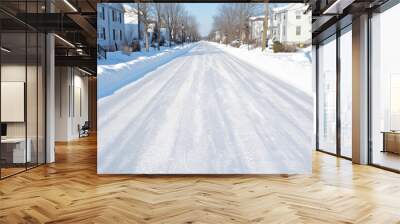 A quiet suburban street blanketed in fresh snow on a clear winter day, with houses and bare trees lining the road Wall mural