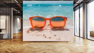 Bright orange sunglasses resting on sandy beach near turquoise water, reflecting ocean waves Wall mural