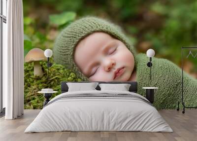 Close-up of a newborn baby wrapped in a green knitted blanket, sleeping peacefully outdoors on a mossy surface with a small mushroom nearby Wall mural