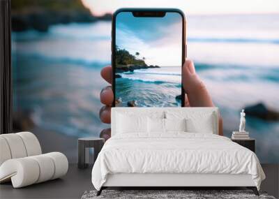 Close-up of a person holding a phone taking a picture of a beautiful tropical beach Wall mural