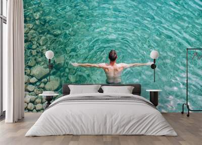 Top view of a man swimming in crystal-clear turquoise water, surrounded by smooth rocks Wall mural