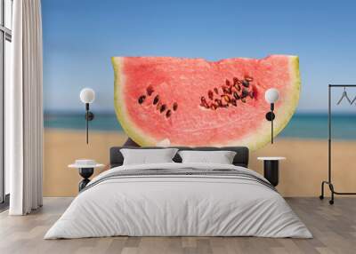 Bitten ripe piece of watermelon in woman hands on the beach in a hot summer day. Concept Wall mural