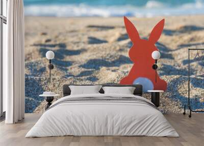 Creative easter concept photo of red paper bunny on the sand on the beach at sunset. Concept. Easter celebrations in tropical countries. Wall mural