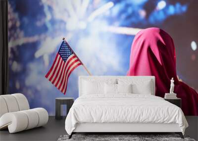 Muslim woman in a scarf holding American flag  during fireworks at night. Wall mural