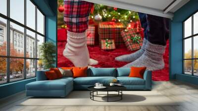 Woman feet standing in tip toe in winter socks near male lags on a fluffy red blanket near a Christmas tree with gifts. Concept Wall mural