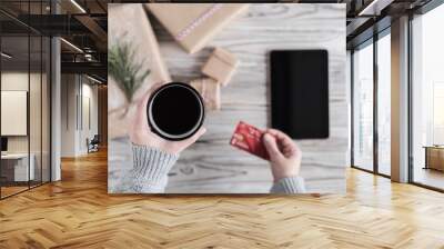 Woman with cup of coffee, credit card and tablet. Packing gifts. Cardboard box in craft paper on the rustic wood planks background. Christmas and New Year concept. Wall mural