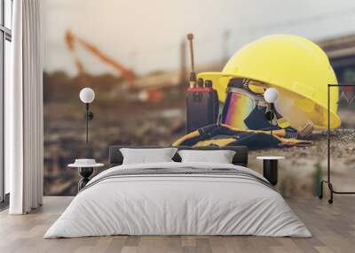 Yellow helmets, gloves, radio communication and safety glasses placed on the cement floor are the background of the construction of blurred buildings. Wall mural