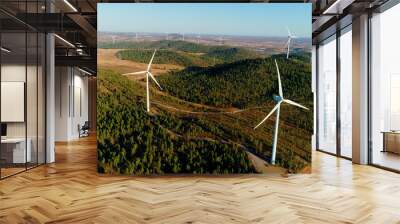 Beautiful wind turbines near pine tree forest under the blue sky. Renewable energy production for the green environmental world - close-up view with a drone - environment & ecological concept Wall mural