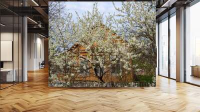 In the foreground are flowering trees, behind them a small village house. Wall mural