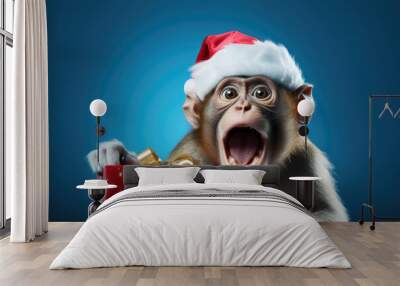 Adorable Young monkey surprised, wearing a Christmas hat. Holding a Christmas present. Posing on blue background, funny looking. Celebrating Christmas concept Wall mural