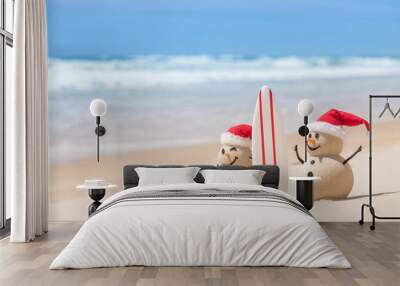 Two Sandy Christmas Snowmen are watching the waves, standing on beautiful beach with a surf board Wall mural