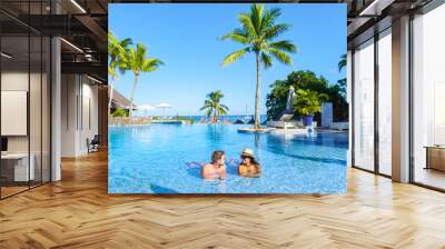 Man and Woman relaxing in a swimming pool, a couple on a honeymoon vacation in Mauritius tanning in the pool with palm trees and sun beds Wall mural