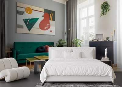 Luxury and modern home interior with design green sofa, navy commode, tables, pouf and accessroies. A lot of plants in the room. Abstract painting.  Stylish decor of living room with brown parquet.  Wall mural